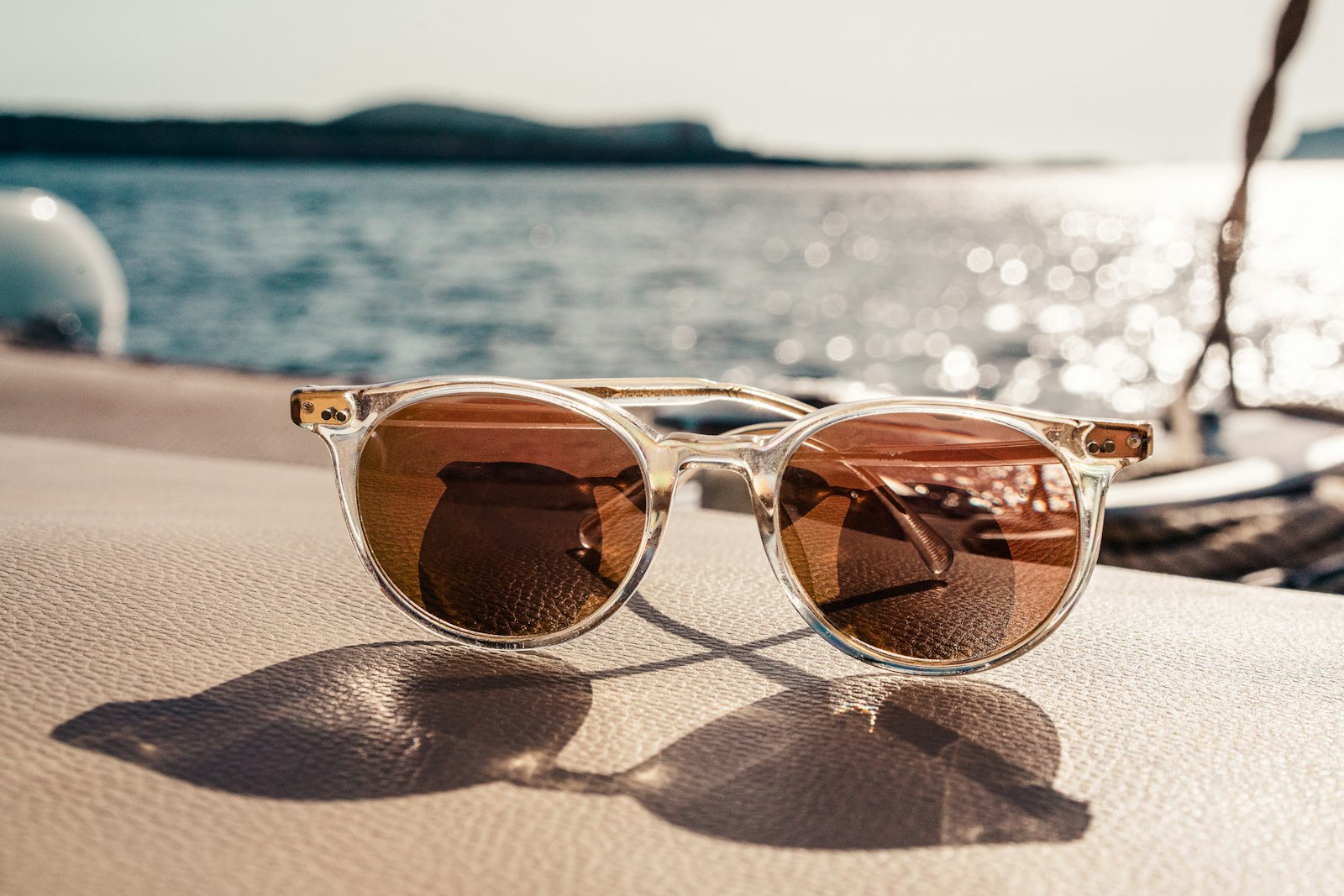 Clear-framed sunglasses with amber lenses on a boat deck, sunlit sea behind